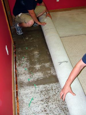 Greene water damaged carpet being removed by two men.